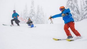 DREAM Adaptive participant and volunteers skiing down a run on a powder day