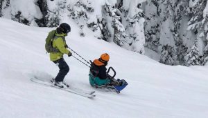 Dream Adaptive Staff assists a skier down a ski run using a sit ski and straps