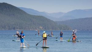 several paddle boarders and volunteers on a lake with mountains in the background