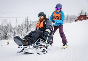 A visually impaired sit-skier is being supported by an instructor.
